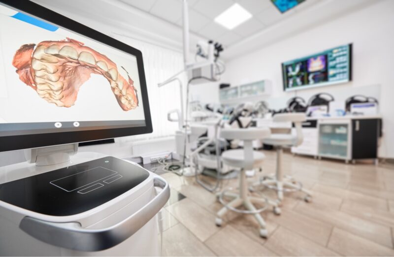 A dental clinic room at Chestnut Dental Needham with a digital screen displaying a 3D dental scan, surrounded by dental chairs and equipment, offering advanced care for Franklin and Bedford patients.